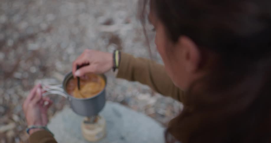 A woman is making soup on a small camping stove