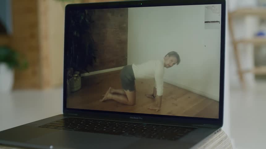 A video of a yoga instructor on a laptop performing a yoga stretch and looking at the camera
