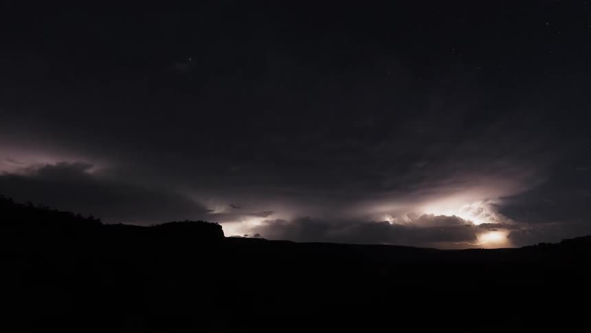 Timelapse of rain and dark lightning storm clouds rolling over a mountain from sunset to night