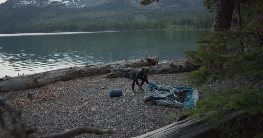 A woman sets up a tent next to a lake