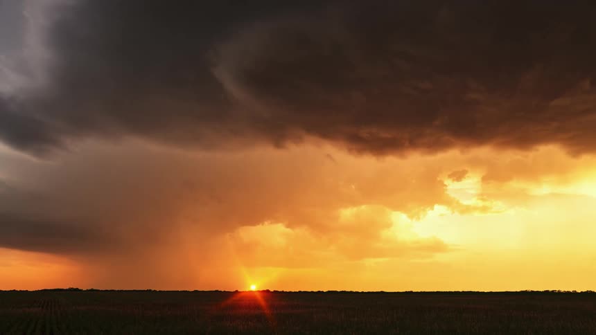 Dark storm clouds move across a bright orange sky as the sun sets