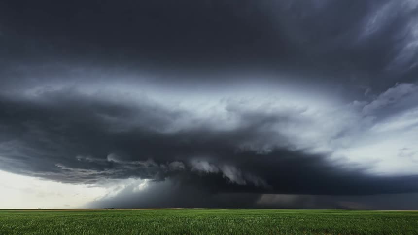 A time lapse shows enormous storm clouds rolling across the sky at sunset while dumping rain on the field below