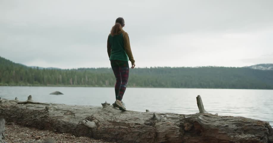 A woman climbing onto a fallen log next to a lake in nature
