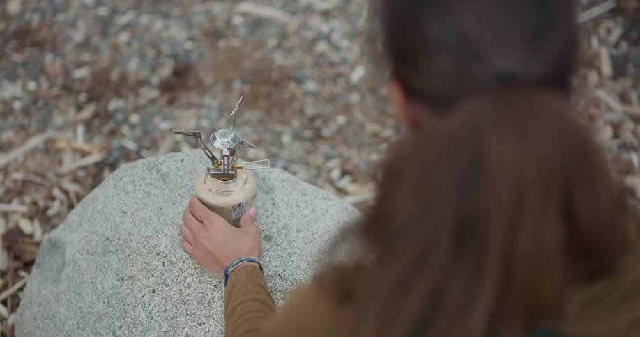 Woman cooking a meal in a small pot over a portable stove while camping