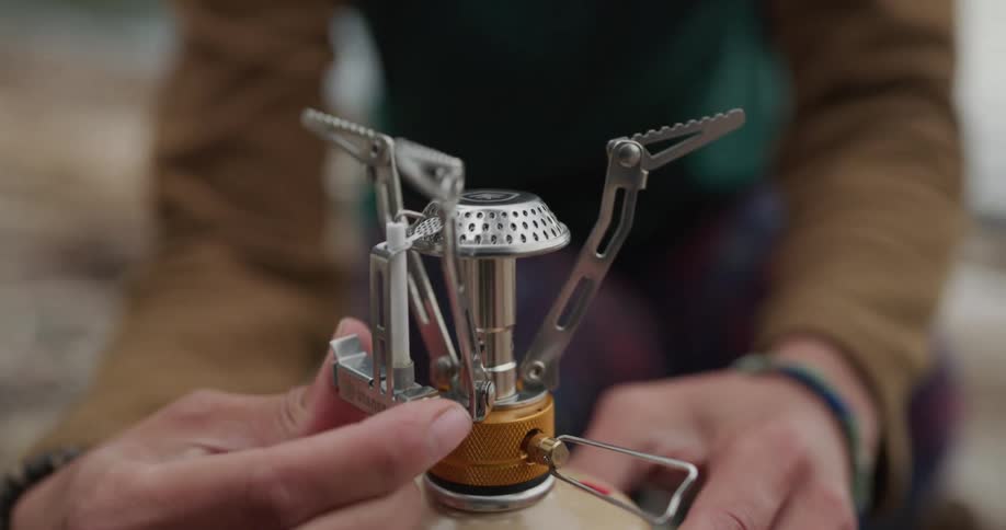 A woman outside lights a flame and puts a pot on top of it