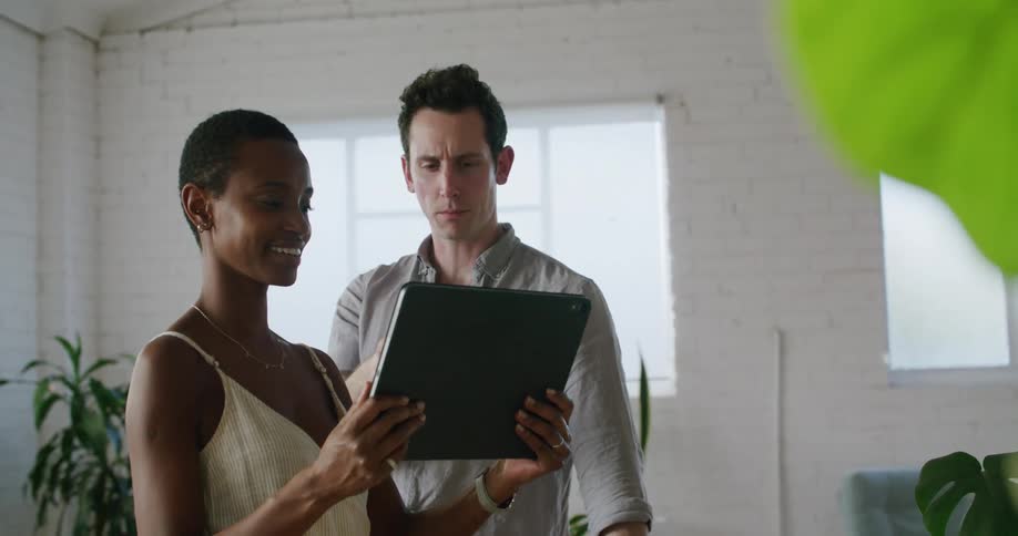 A man and woman in an office talk as they look at a tablet