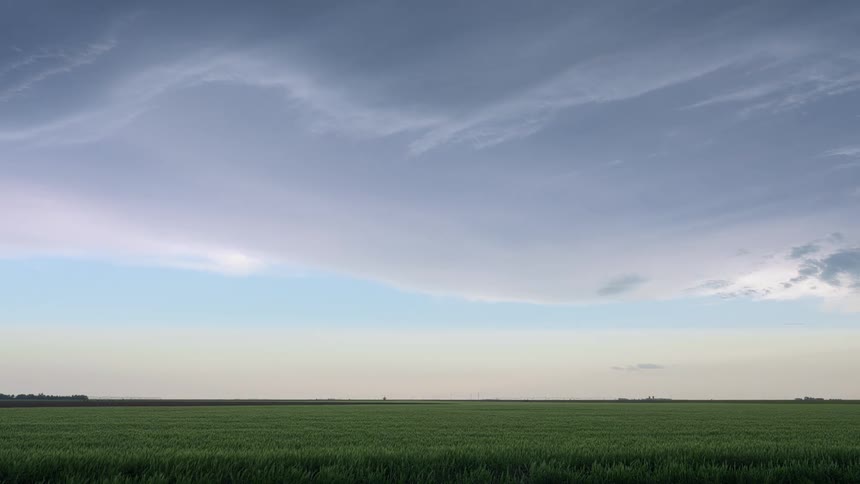Timelapse of storm clouds calmly flowing over the green grass on a field at morning