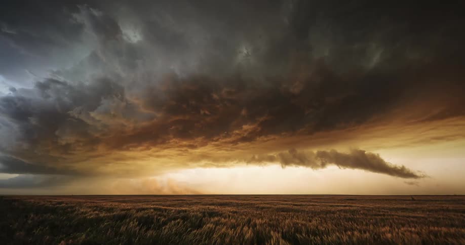 Dark storm clouds move over farmland in an orange sky