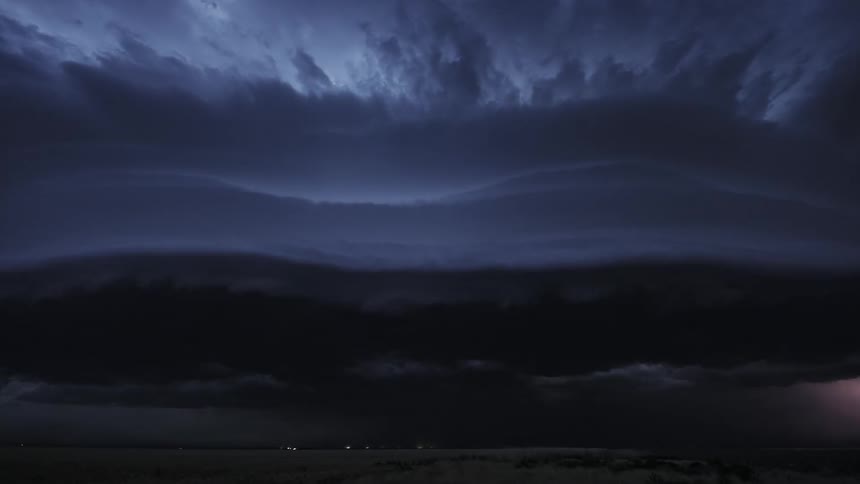 Timelapse of lightning and dark storm clouds rolling over a field at night