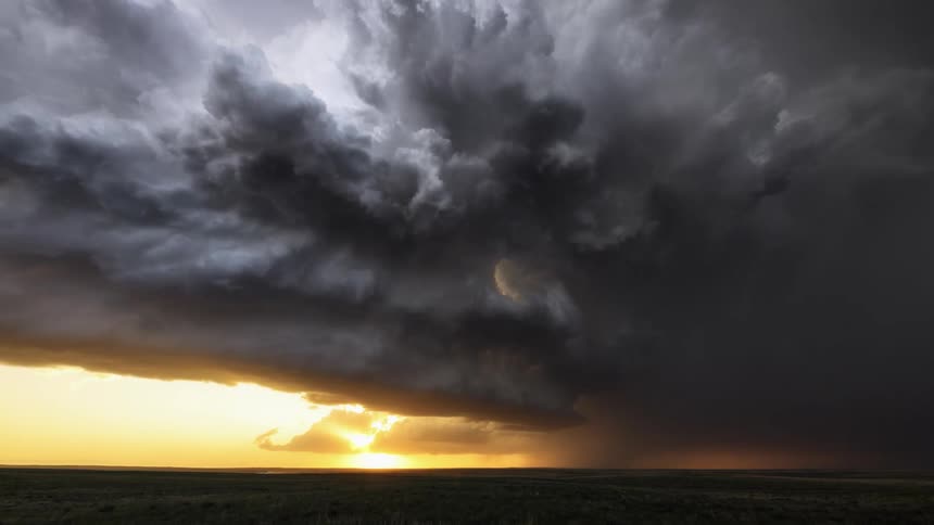 Timelapse of rain and dark storm clouds rolling over a field at sunset
