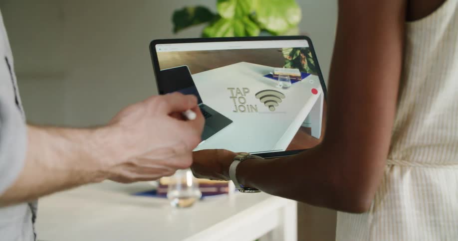 A man and woman stand in an office and look at a tablet as the man taps on it