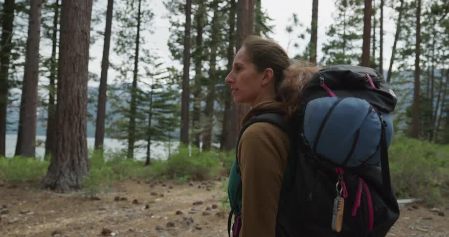 Woman wearing a backpack walking on a trail through the pine tree forest near a lake