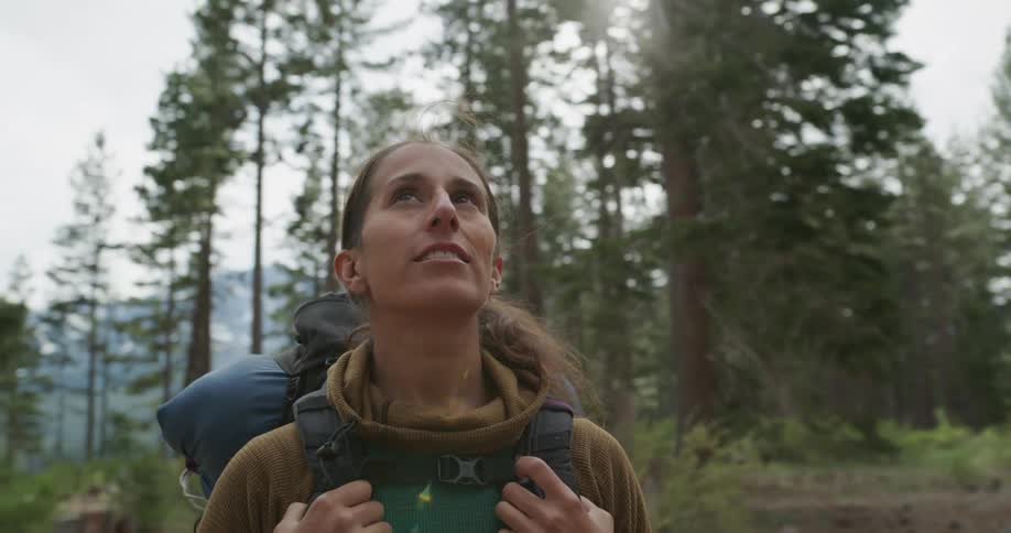 A woman with a backpack on stands in a forest and looks around