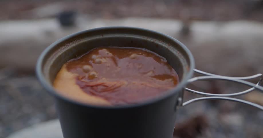 Boiling meal in a small pot over a portable stove in a campsite