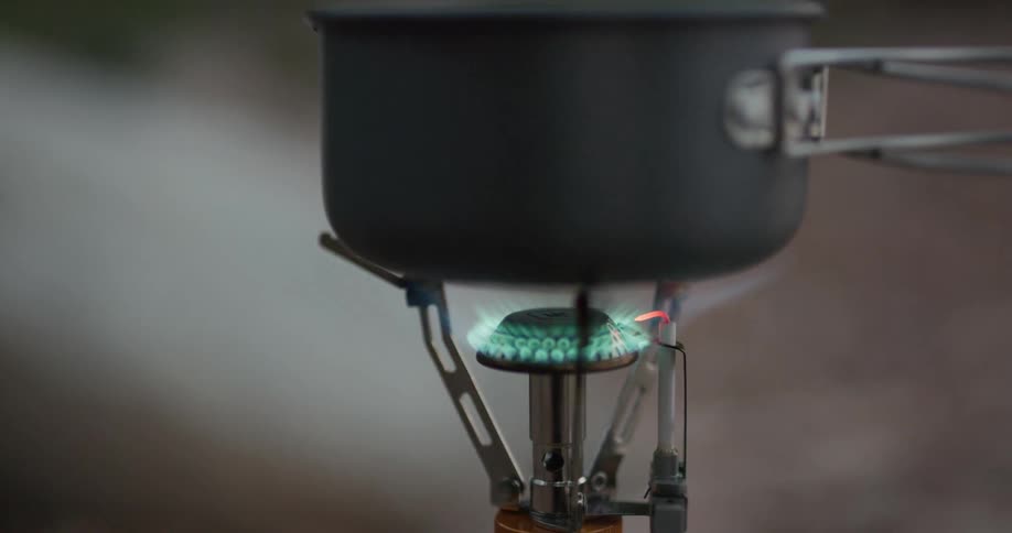 Cooking a meal in a small pot over a portable stove while camping