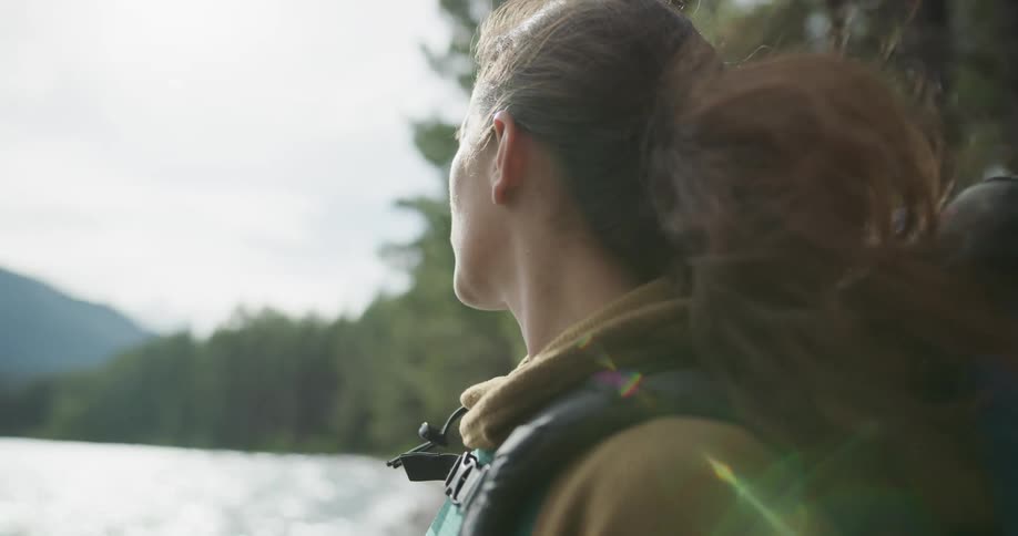 A woman staring off towards a lake in a forest smiles and scans the area at daytime