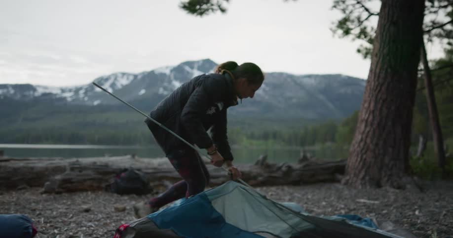 A woman assembling a tent in a forest