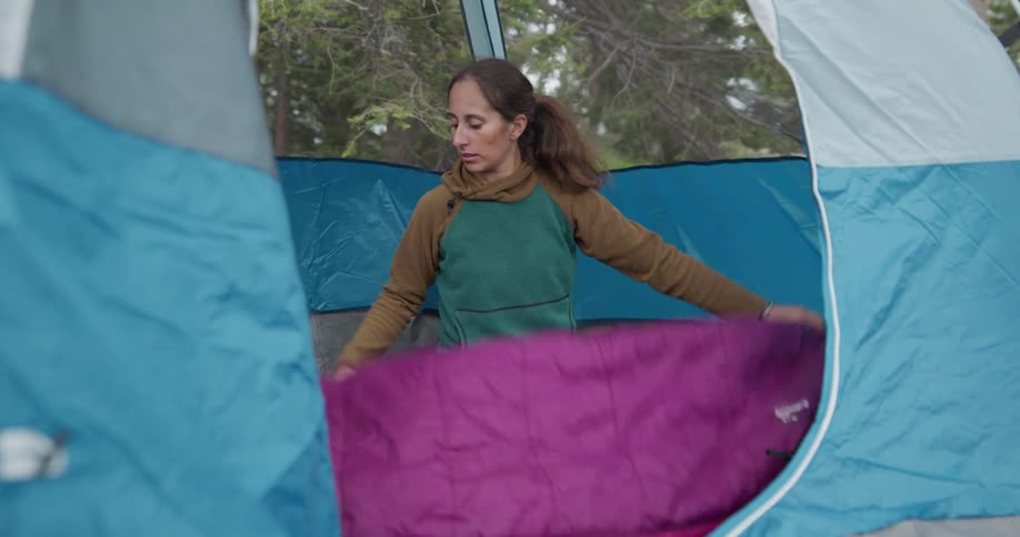 A woman in a tent takes a sleeping bag out of a bag