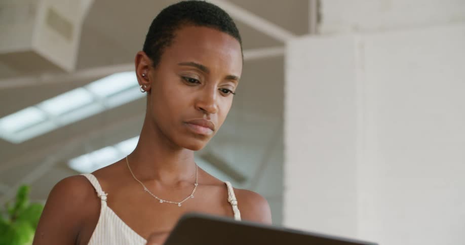 A woman wearing a white dress stands in a white office working on a tablet