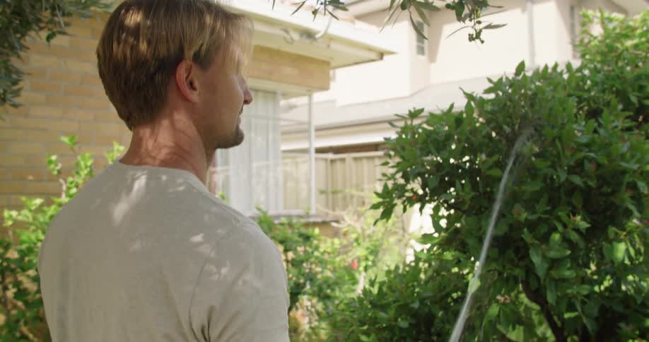 A man waters a tree in his back yard