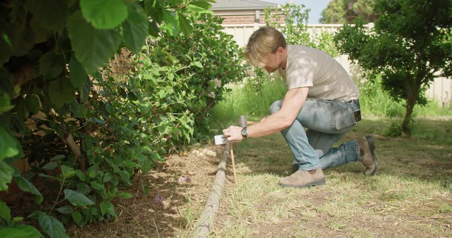 Man hammers wooden stake into ground near plant bed