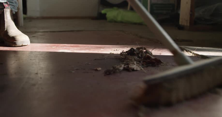 A person wearing boots sweeping the floor of a room using a broom