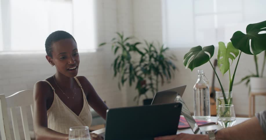 Man with a shirt and woman with short hair and a white sleeveless shirt use a tablet and a laptop