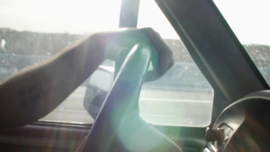 A person using the steering wheel of a car to drive in the highway at sunset