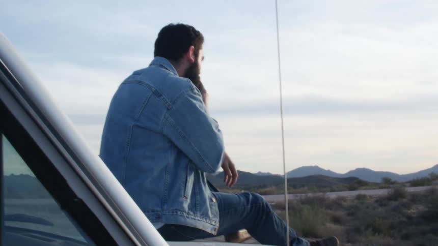 A man that is sitting on the hood of a car