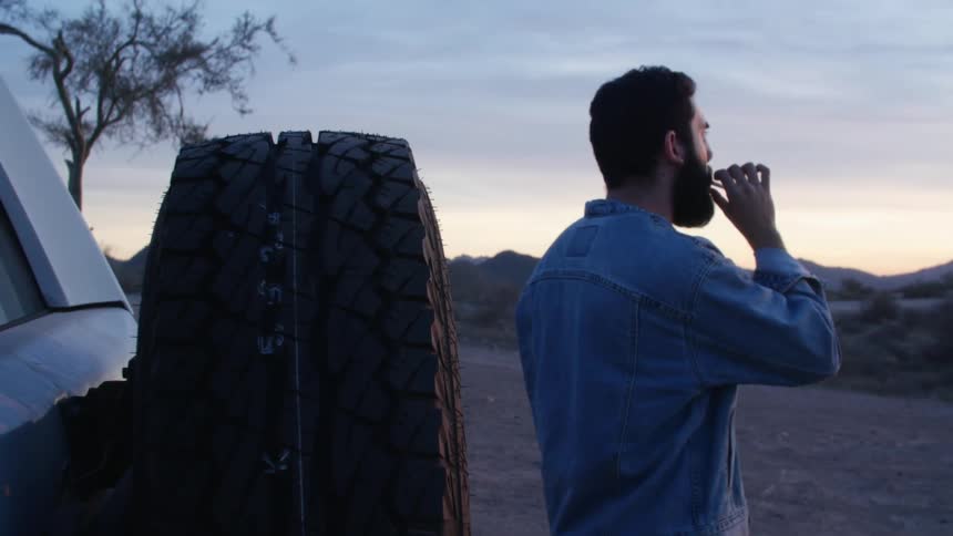 A man stands next to his truck smoking a cigarette and looking out at the landscape