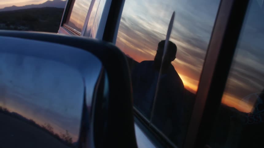 A man is standing by his car outdoors at dusk