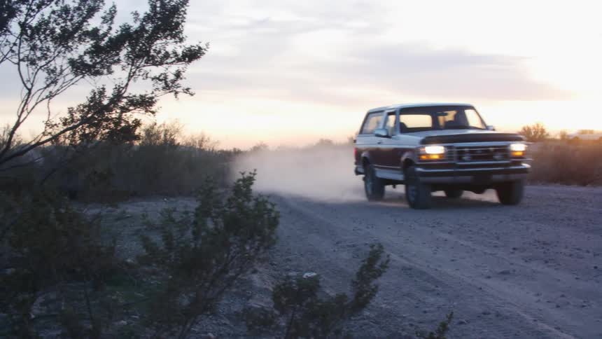 Person drives truck along dirt road through countryside with sun sitting on horizon