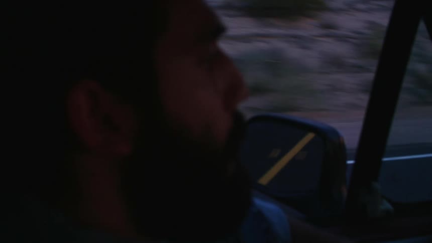 Man drives through scrub while side mirror reflects road