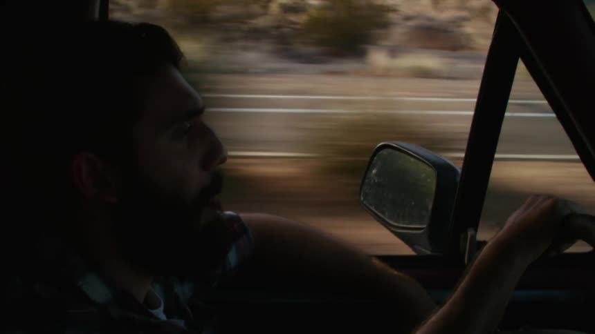 A bearded man driving on a paved road in the daytime