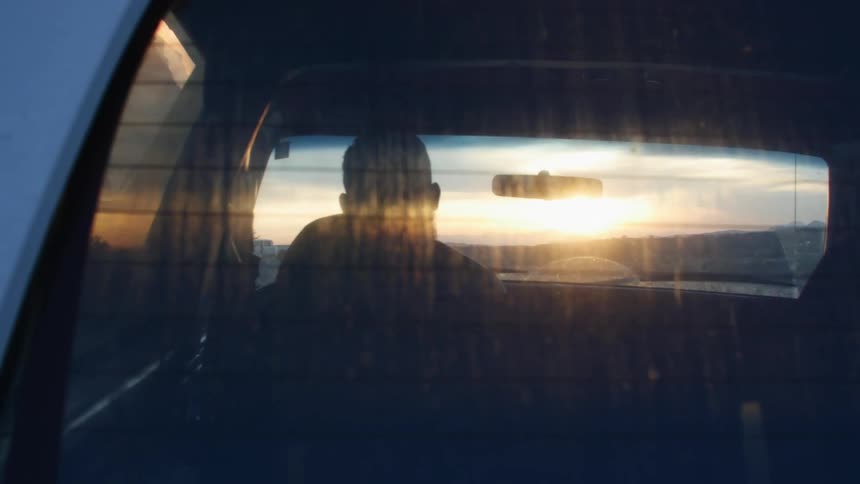 A man is driving a car at sunset