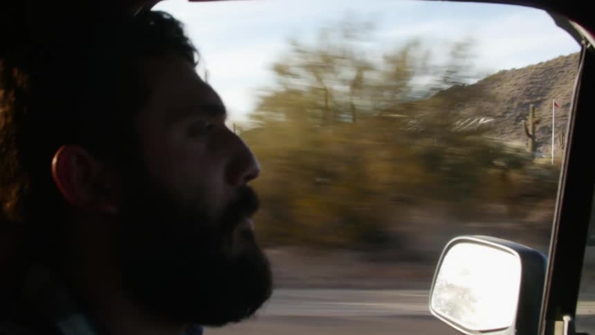 Bearded man driving a pickup truck on a rural road at evening