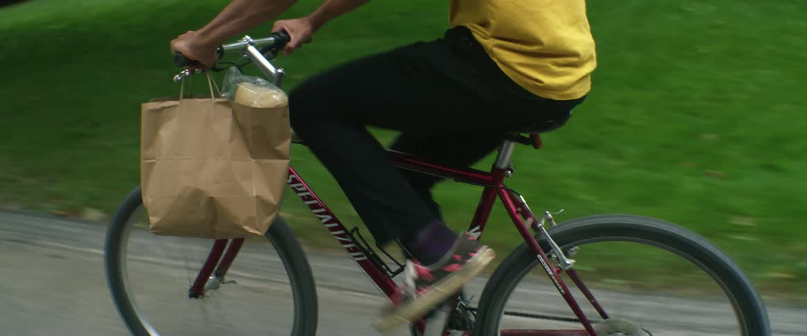 Young man carries a grocery bag while driving a bicycle on the streets of a neighborhood