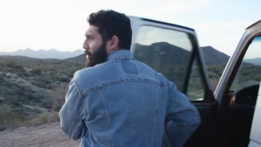 A man climbs out of a vehicle parked in the countryside and looks around at the surroundings