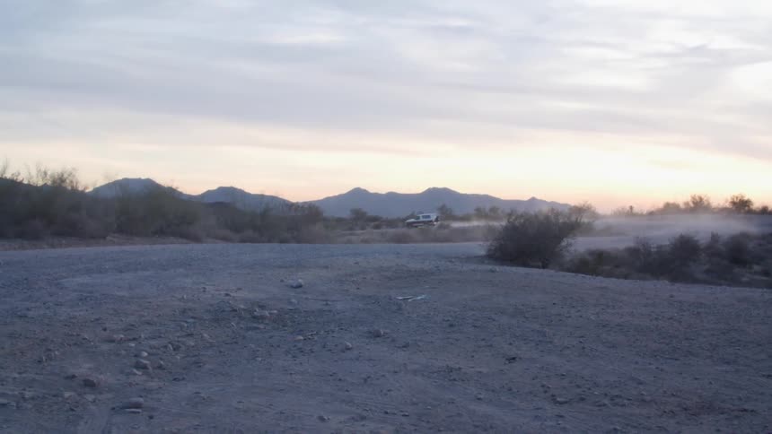 A white sport utility vehicle drives along a curve of a dirt road near a desert canyon