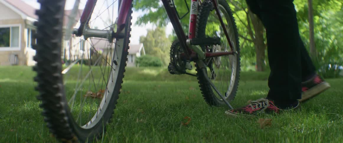 A person stops their bike on the lawn and walks away
