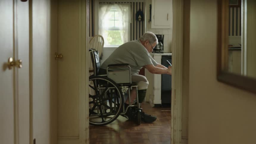 Elderly man on a wheelchair sweeping the floor with a broom at home