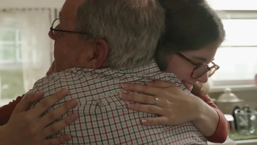 A woman hugs an elderly man in a home kitchen during the day