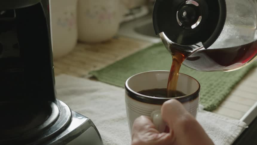 A person pouring coffee into a ceramic mug in a home kitchen