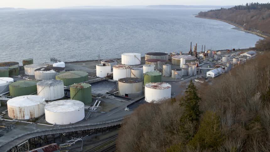 Multiple old and rusty storage tanks in an industrial yard along the coast