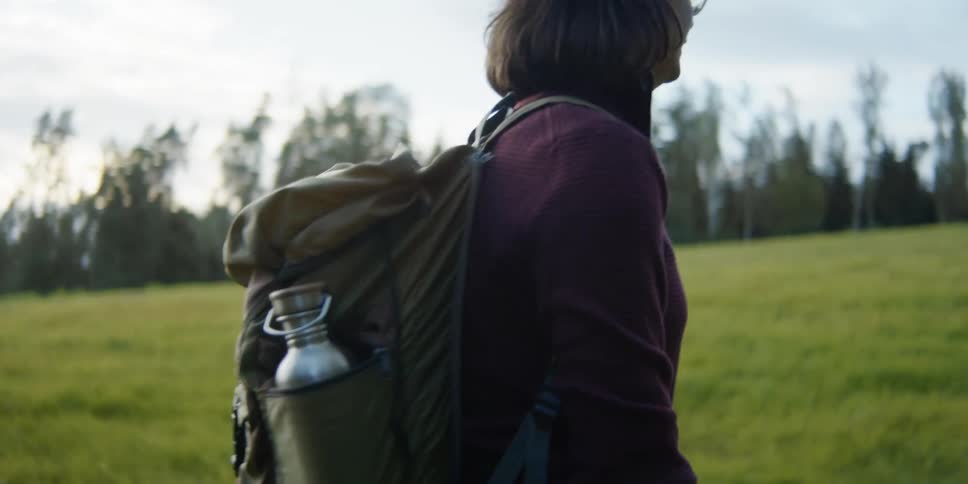 Lesbian couple holding hands walks on a trail next to trees in the field