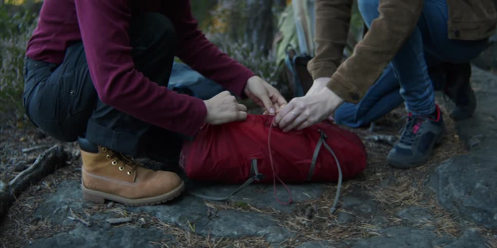 Two women in a forest tying a back pack