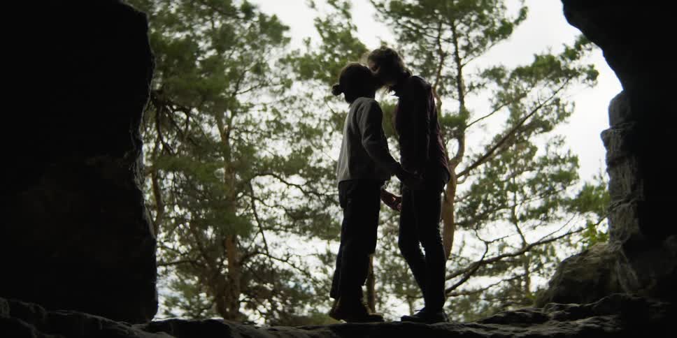 Two women kiss by a cave entrance