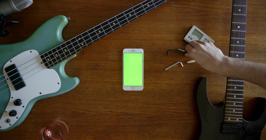 A person picks up and uses tools on a guitar lying on a table