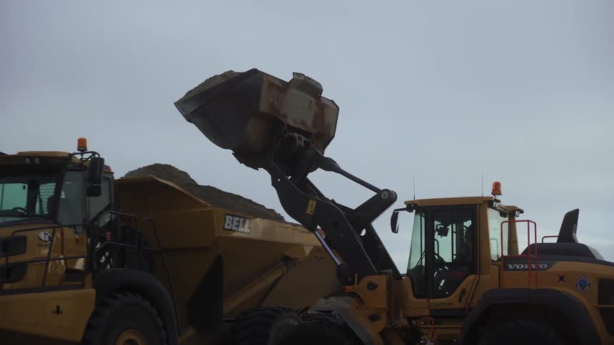 A front end loader unloading sand on a dump truck near the ocean