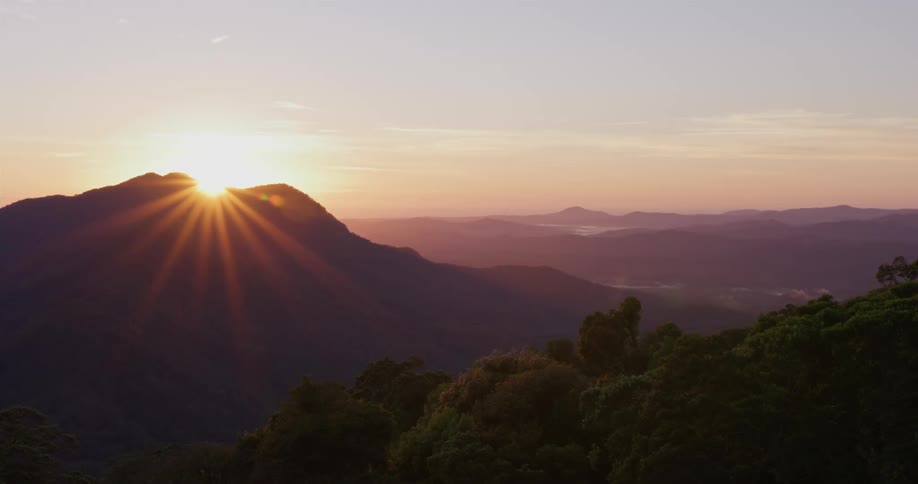 Sun rises over mountain peak between forest and mist covered mountains under red sky